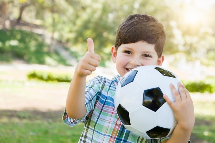 Cute young boy playing with soccer ball and thumbs up outdoors in the park, Photo by Andy Dean