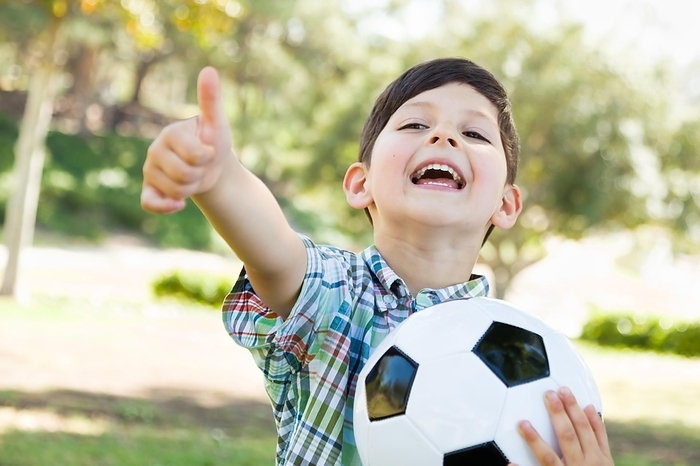 Cute young boy playing with soccer ball and thumbs up outdoors in the park, Photo by Andy Dean