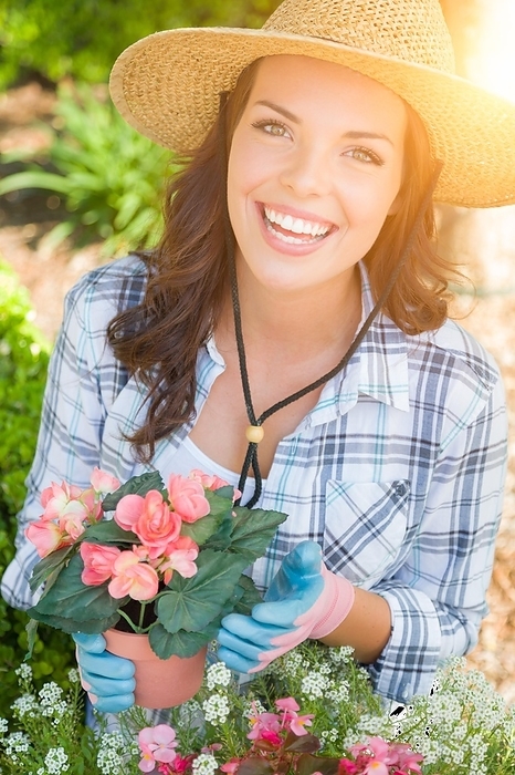 Happy young adult woman wearing hat and gloves gardening outdoors, Photo by Andy Dean