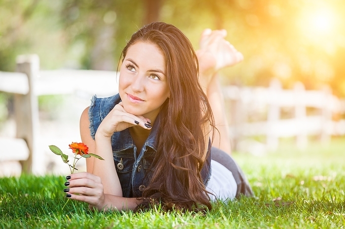 Attractive mixed-race girl daydreaming laying in grass outdoors with flower, Photo by Andy Dean