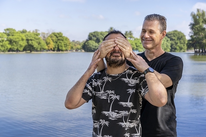 Couple of mature gay men, one surprising the other by covering his eyes in a lake. Concept of surprise, happiness, game, Photo by Mariano Gaspar