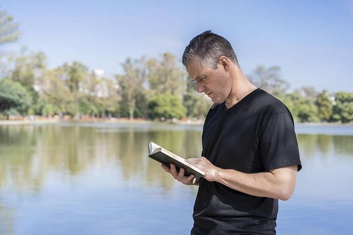 Mature man reading by a lake, enjoying free time on a sunny day, Photo by Mariano Gaspar