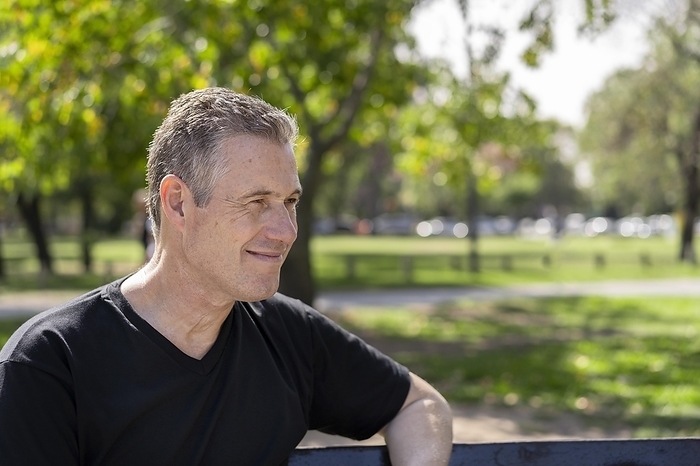 Close-up portrait of a mature man with gray hair wearing a black t-shirt sitting on a park bench looking to the side, Photo by Mariano Gaspar