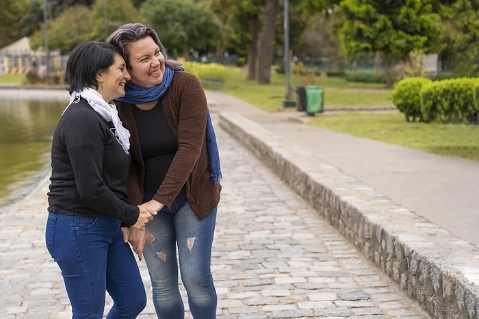 Lesbian couple in a park holding hands laughing. Copy space, Photo by Mariano Gaspar