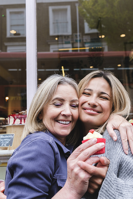 Smiling mother and daughter with cupcake embracing outside store