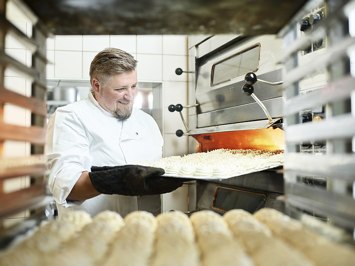 Happy confectioner taking out tray from oven at kitchen