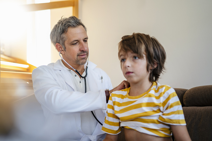 Doctor with stethoscope examining boy at home