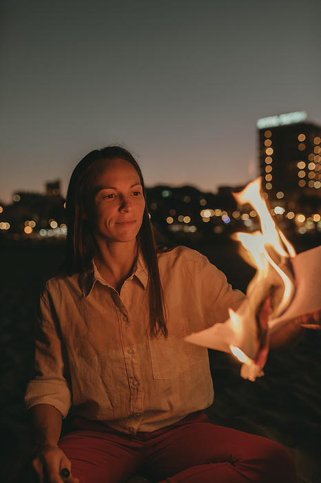 Woman burning paper on beach at night
