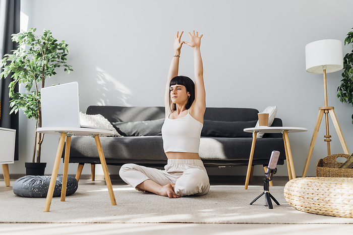 Woman with arms raised doing online yoga in front of laptop at home