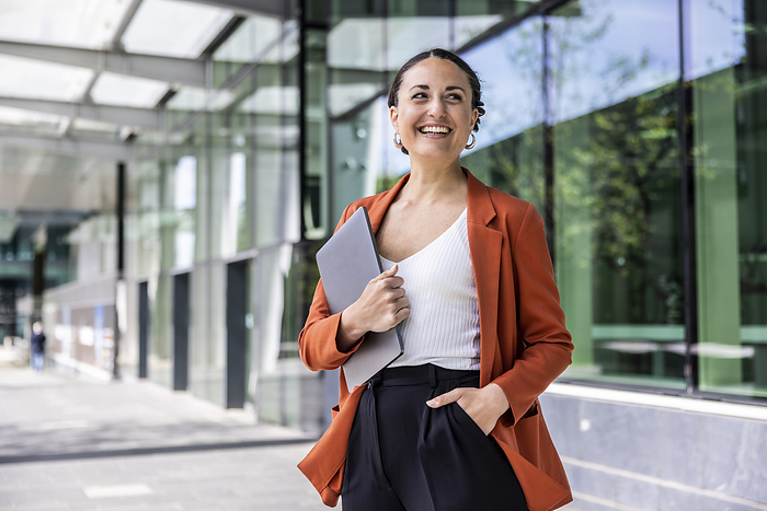Smiling businesswoman holding laptop standing with hand in pocket