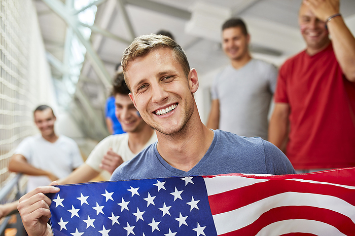 Happy man holding American Flag with by friends at sports event in stadium