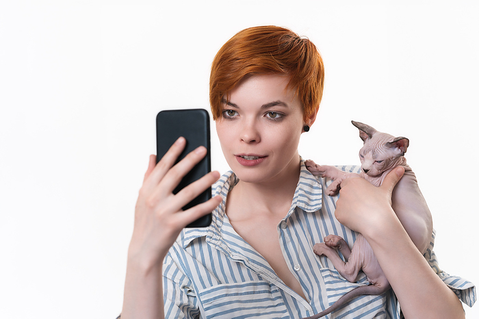 Woman hugging cat, having video-call holding smart phone in hand shooting selfie on front camera