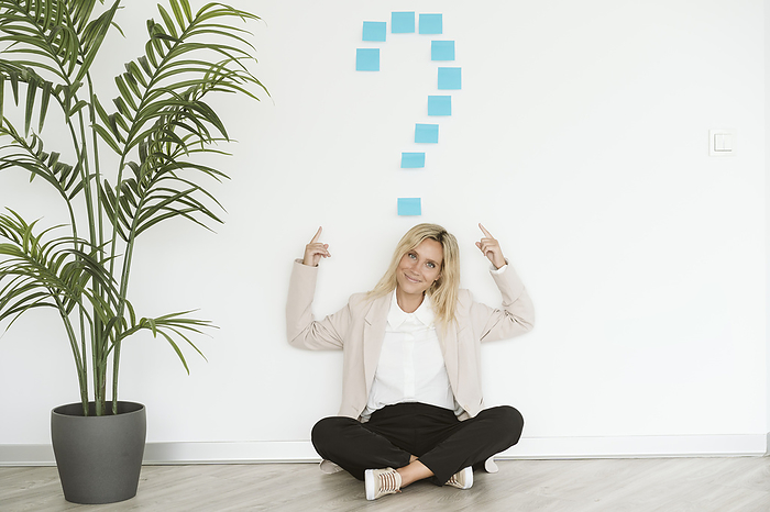 Businesswoman sitting on the floor in office pointing at question mark above her, Photo by Eva Blanco