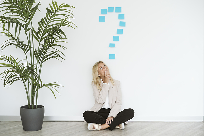 Businesswoman sitting on the floor in office with question mark above her, Photo by Eva Blanco
