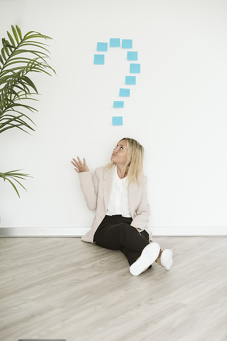 Businesswoman sitting on the floor in office looking at question mark above her, Photo by Eva Blanco