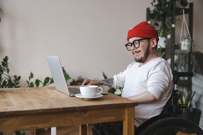 Smiling man in wheelchair using laptop at home, Photo by Gerasimovi
