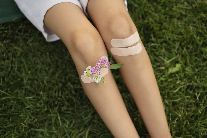 Girl with knees taped by bandage and flowers sitting on grass, Photo by Lily Solopova