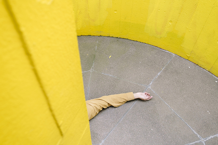 Hand of unconscious man on floor by yellow wall