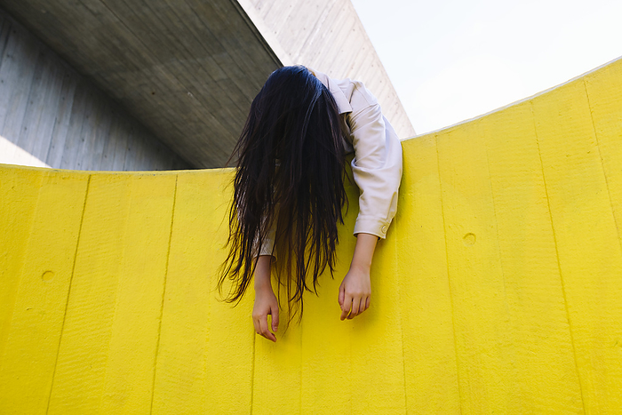 Unconscious young woman leaning on yellow wall