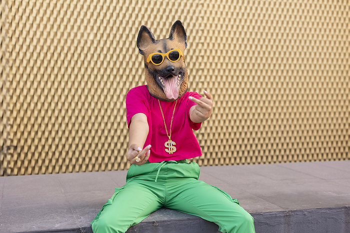 Woman wearing dog mask gesturing middle finger sitting on wall