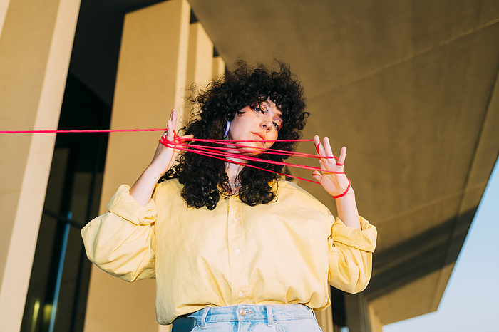 Curly hair woman playing cats cradle with thread