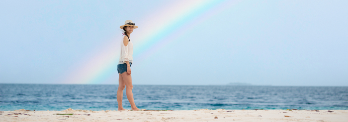 Woman walking on a beach with a rainbow