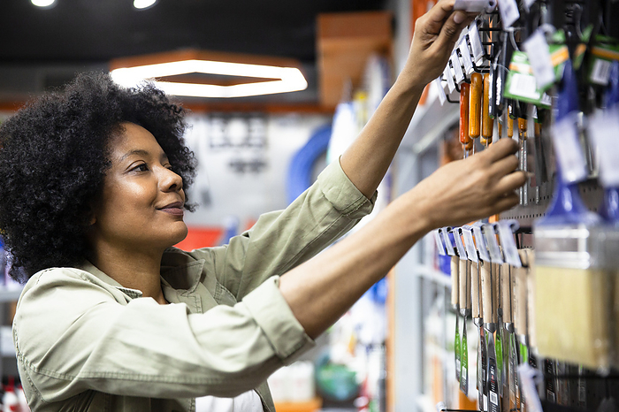 African American female hardware shop owner sorting out products on rack