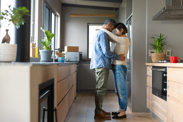 Happy diverse couple dancing together and smiling in kitchen. Spending quality time together at home.