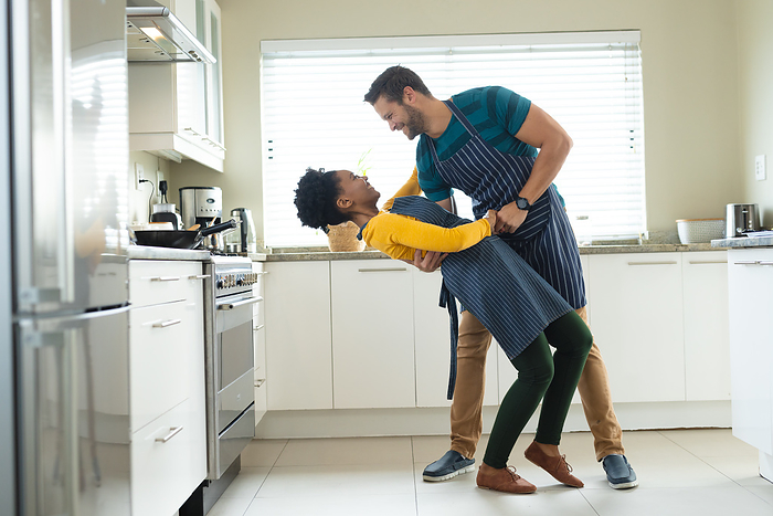 Image of happy diverse couple dancing in kitchen. Love, romantic relationship and spending quality time together concept.