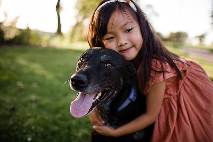 Six Year Old Asian Girl Hugging Black Lab at Park in San Diego