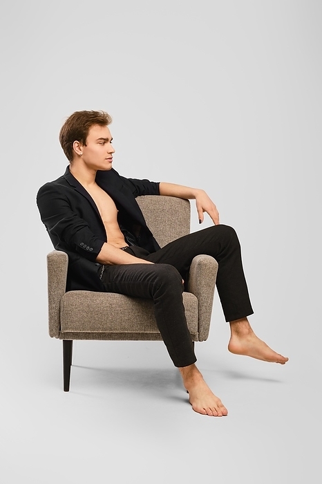 Happy young man in black suit siting in an armchair in the studio, Photo by Aleksei Isachenko