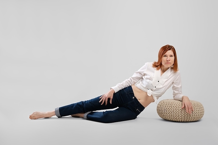 Barefoot middle age woman leaning on padded stool. Studio concept of carefree life, Photo by Aleksei Isachenko