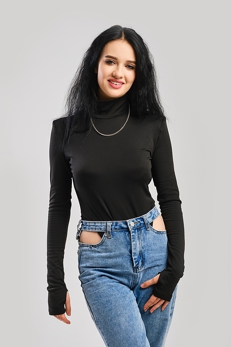 Young happy woman posing in studio in black bodysuit with long sleeves and oversized jean over grey background, Photo by Aleksei Isachenko