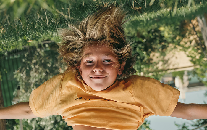 Kid hanging upside down while playing outdoors at backyard.