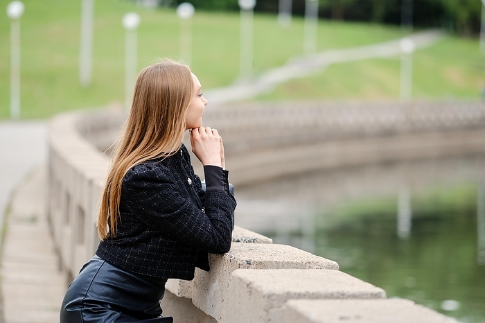 Young woman leans against the railing and looks thoughtfully at the river, Photo by Aleksei Isachenko