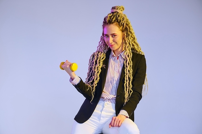 Woman power concept, girl in jeans and jacket with dreadlocks pumps dumbbell, Photo by Aleksei Isachenko
