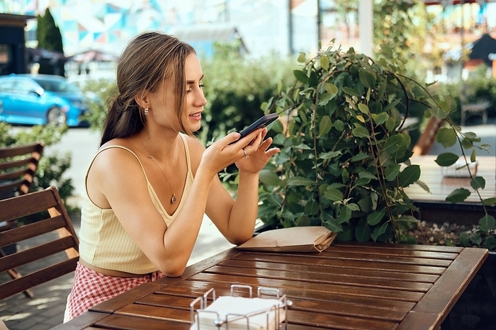 Young woman makes online phone call while sitting at outdoor terrace, Photo by Aleksei Isachenko