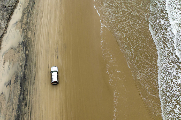 Aerial view of an SUV parked on beach road with waves