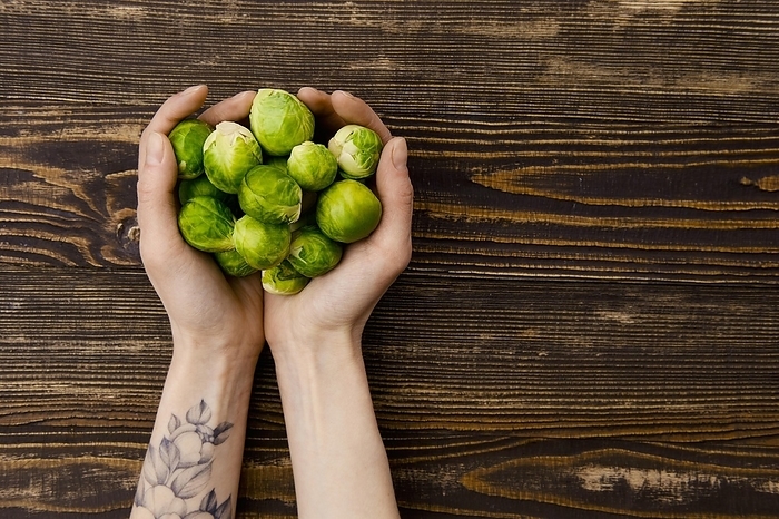 Overhead view of fresh brussel sprout in hands over wooden background, Photo by Aleksei Isachenko