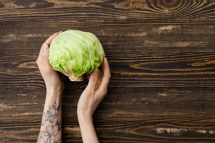 Overhead view of fresh iceberg lettuce in hands over wooden background, Photo by Aleksei Isachenko