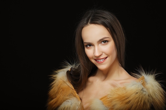 Portrait of beautiful happy girl with natural makeup in fluffy fur coat on black background, Photo by Aleksei Isachenko