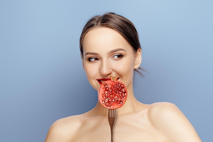 Beautiful fashion model with perfect skin, natural makeup and red lips with pomegranate isolated on blue background, Photo by Aleksei Isachenko
