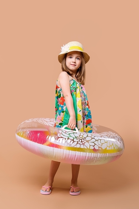 Cute child in sundress and straw hat with swimming ring playing in studio, Photo by Aleksei Isachenko