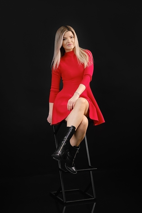 Pretty woman in red dress sitting on chair in dark studio, Photo by Aleksei Isachenko