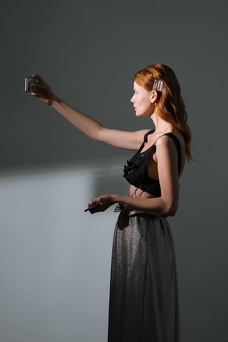 Pretty girl take a self portrait with her mobile. Fashion model making selfie on smartphone over gray background, Photo by Aleksei Isachenko