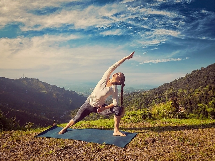 Vintage retro effect hipster style image of sporty fit woman practices yoga asana Utthita Parsvakonasana, extended side angle pose outdoors in mountains in the morning, Photo by Dmitry Rukhlenko