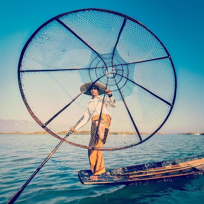 Vintage retro effect filtered hipster style image of Myanmar travel attraction. Traditional Burmese fisherman with fishing net at Inle lake famous for their distinctive one legged rowing style, Photo by Dmitry Rukhlenko