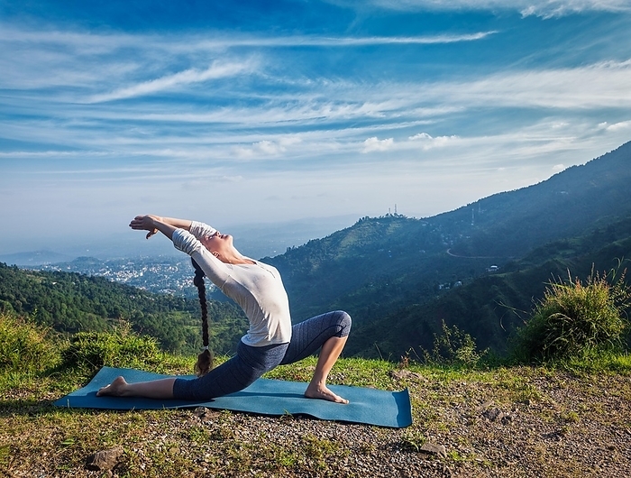 Sporty fit woman practices yoga Anjaneyasana, low crescent lunge pose outdoors in mountains in morning, Photo by Dmitry Rukhlenko
