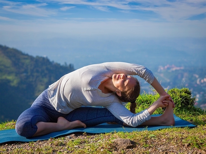 Yoga outdoors, young sporty fit woman doing Hatha Yoga asana parivritta janu sirsasana, Revolved Head-to-Knee Pose, in mountains in the morning, Photo by Dmitry Rukhlenko