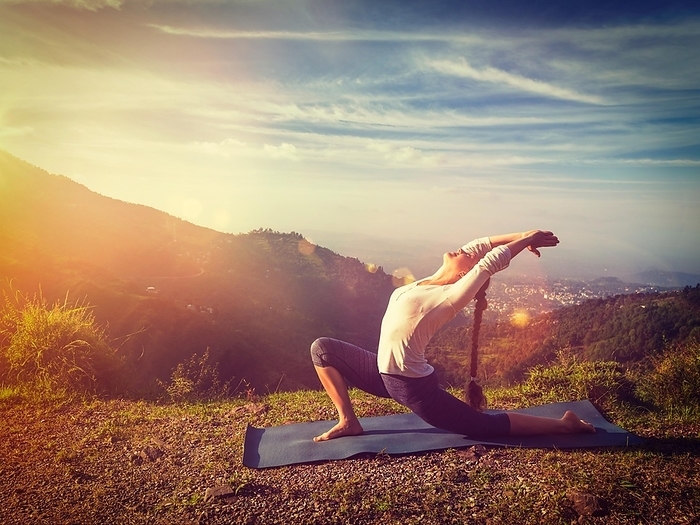 Yoga outdoors, sporty fit woman practices yoga Anjaneyasana, low crescent lunge pose outdoors in mountains in morning. With light leak and lens flare. Vintage retro effect filtered hipster style image, Photo by Dmitry Rukhlenko